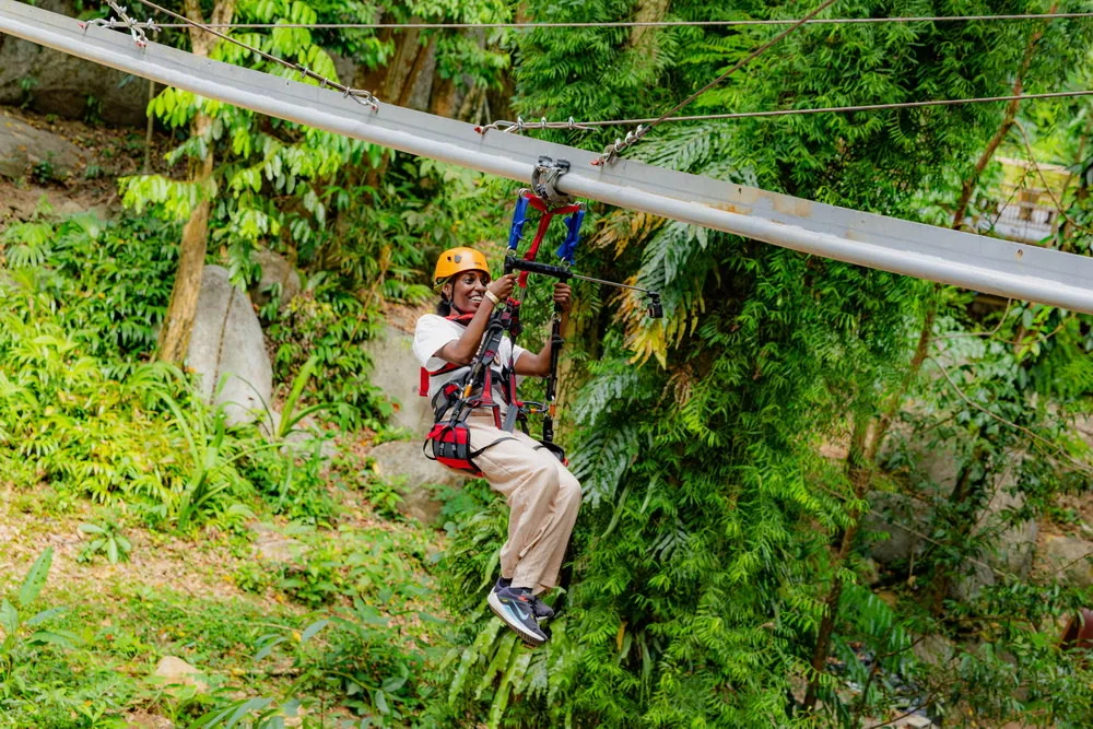 A helmeted rider suspended beneath the roller track among trees
