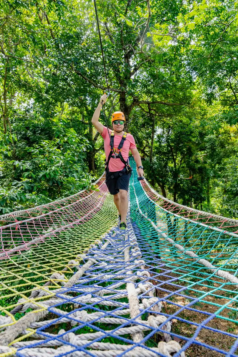 Helmeted participant on a colourful suspension bridge in the forest