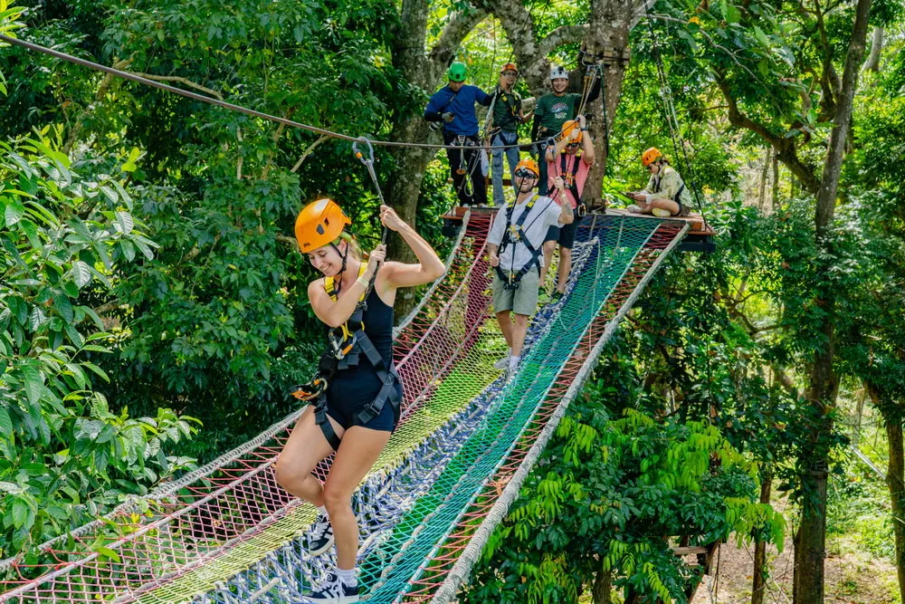 Helmeted visitors crossing a colourful suspension bridge at Sky Rock